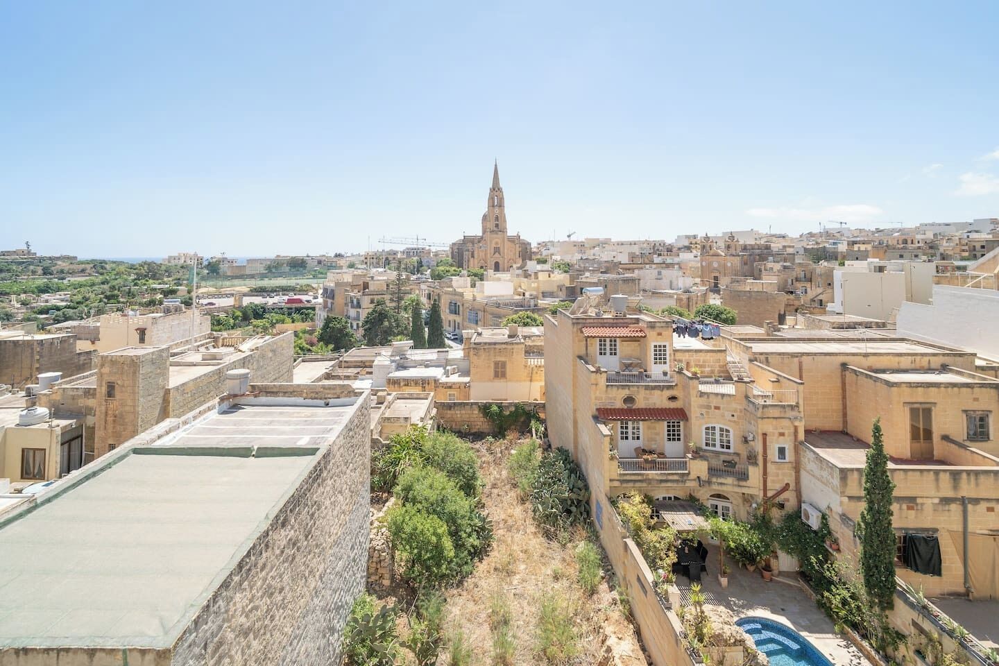 Un paisaje urbano con una imponente aguja de iglesia, edificios residenciales densos y una azotea con piscina.