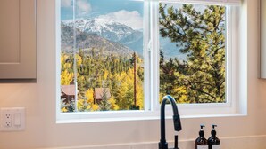 Een badkamer met een raam dat uitkijkt op een bergachtig landschap en herfstkleuren.