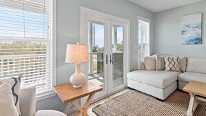 A modern living room with a sectional sofa, a small wooden table, and a lamp. - Toes In The Water on 30a!  4-bed directly on 30a!  Steps to pool and beach. (Panama City Beach)