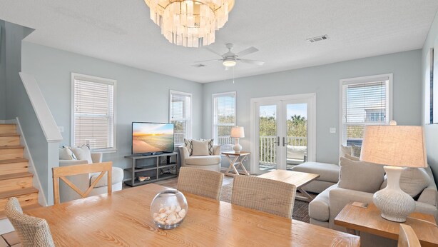 A spacious living room with a wooden dining table, comfortable seating, a television, and a balcony with sliding doors. - Toes In The Water on 30a!  4-bed directly on 30a!  Steps to pool and beach. (Panama City Beach)