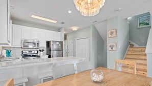 A modern kitchen with white cabinetry, stainless steel appliances, and a wooden dining table. - Toes In The Water on 30a!  4-bed directly on 30a!  Steps to pool and beach. (Panama City Beach)