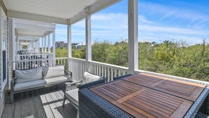 A covered outdoor deck with a sofa and table, overlooking dense greenery. - Toes In The Water on 30a!  4-bed directly on 30a!  Steps to pool and beach. (Panama City Beach)