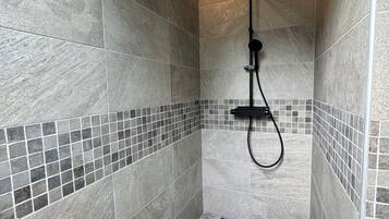 Une douche avec un sol et des murs carrelés, une douchette à main et un luminaire fixé au mur.