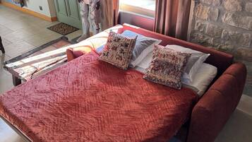 A bed with a red quilt and patterned pillows, a stone wall, and a green door.