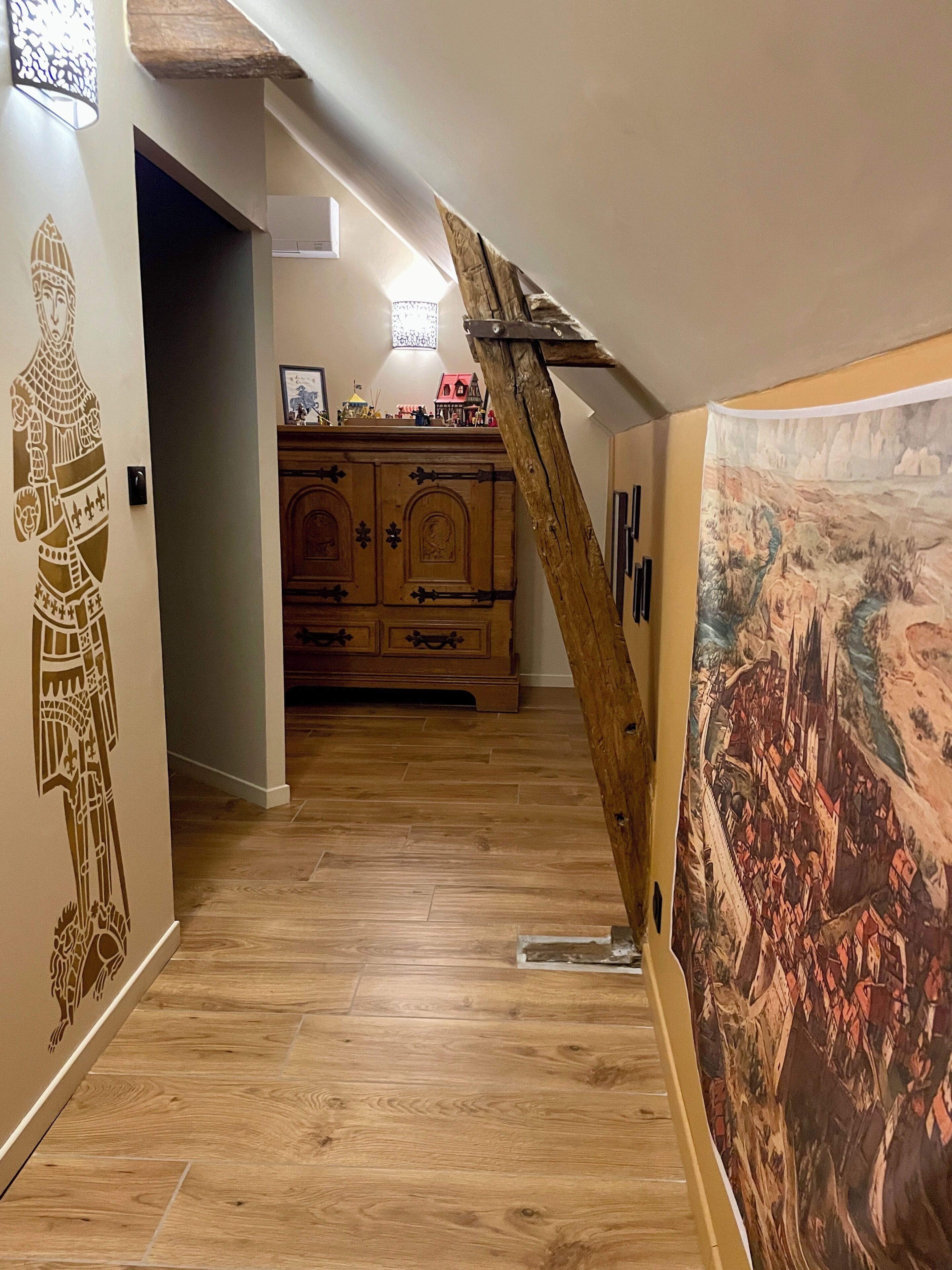 Un escalier en bois avec une rampe en bois, un meuble en bois doté de tiroirs et un mur orné d’une fresque.