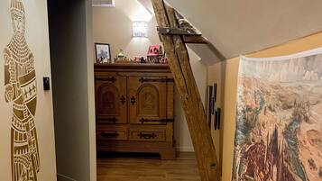 Un escalier en bois avec une rampe en bois, un meuble en bois doté de tiroirs et un mur orné d’une fresque.