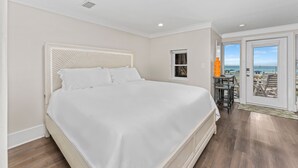 Ein Schlafzimmer mit einem großen Bett, einem kleinen Tisch mit Lampe und Blick auf das Meer durch eine Tür.