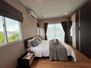 A modern bedroom with a large bed, a bedside table with a vase, and a view of greenery outside. - 3-bedroom villa & 15 min to Bangtao beach (  ตำบล เทพกระษัตรี)