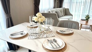 Una mesa de comedor dispuesta con platos blancos, cubiertos y un jarrón con flores blancas.
