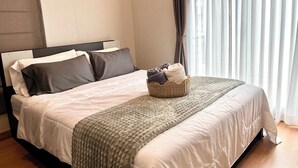 Una cama bien hecha con un edredón gris, una cesta de toallas y un cabecero.