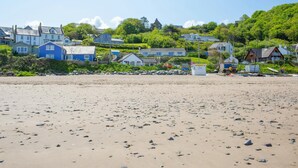 Een strand met verspreide rotsen en huizen op de achtergrond.