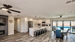A modern kitchen with a central island, bar stools, and a dining area with a pool view.