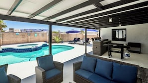 A covered outdoor area with a swimming pool, wicker furniture, and a TV.