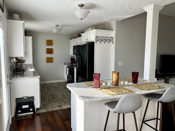 A modern kitchen with white cabinetry, a black refrigerator, and a marble island with bar stools.