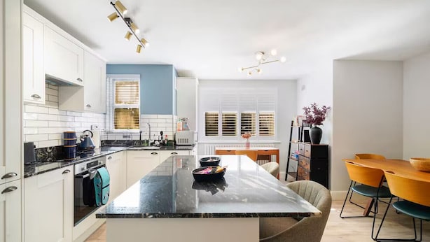 Una cucina moderna con mobili bianchi, un piano di lavoro nero e un'isola centrale. È presente una zona pranzo con un tavolo in legno e sedie arancioni.