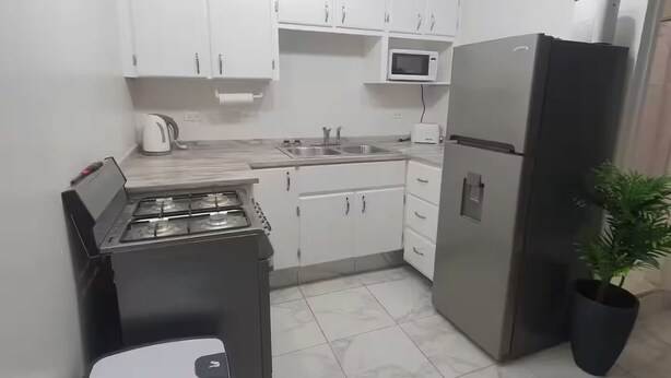 A compact kitchen with white cabinets, a microwave, a refrigerator, a gas stove, and a trash bin.