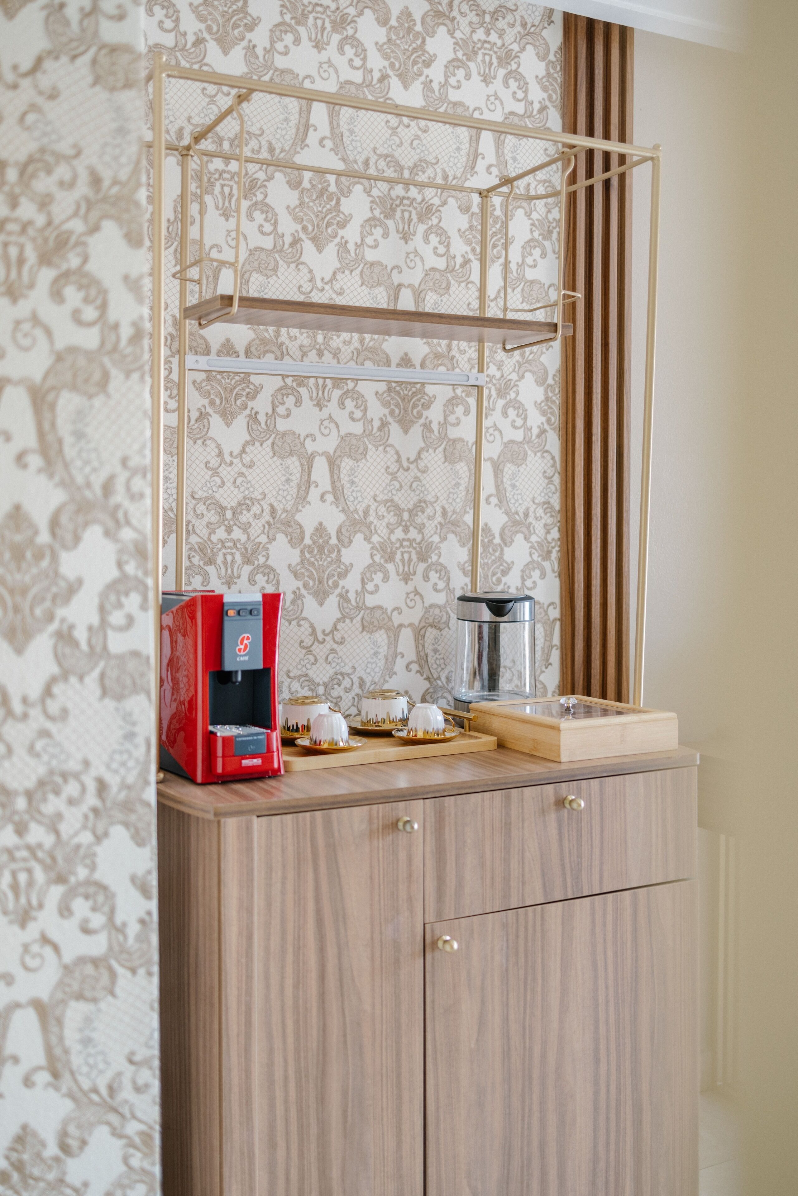 A kitchenette with a coffee machine, a glass carafe, and a wooden cabinet.
