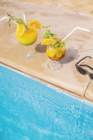 Dos cócteles con pajitas y adornos sobre una mesa junto a una piscina.