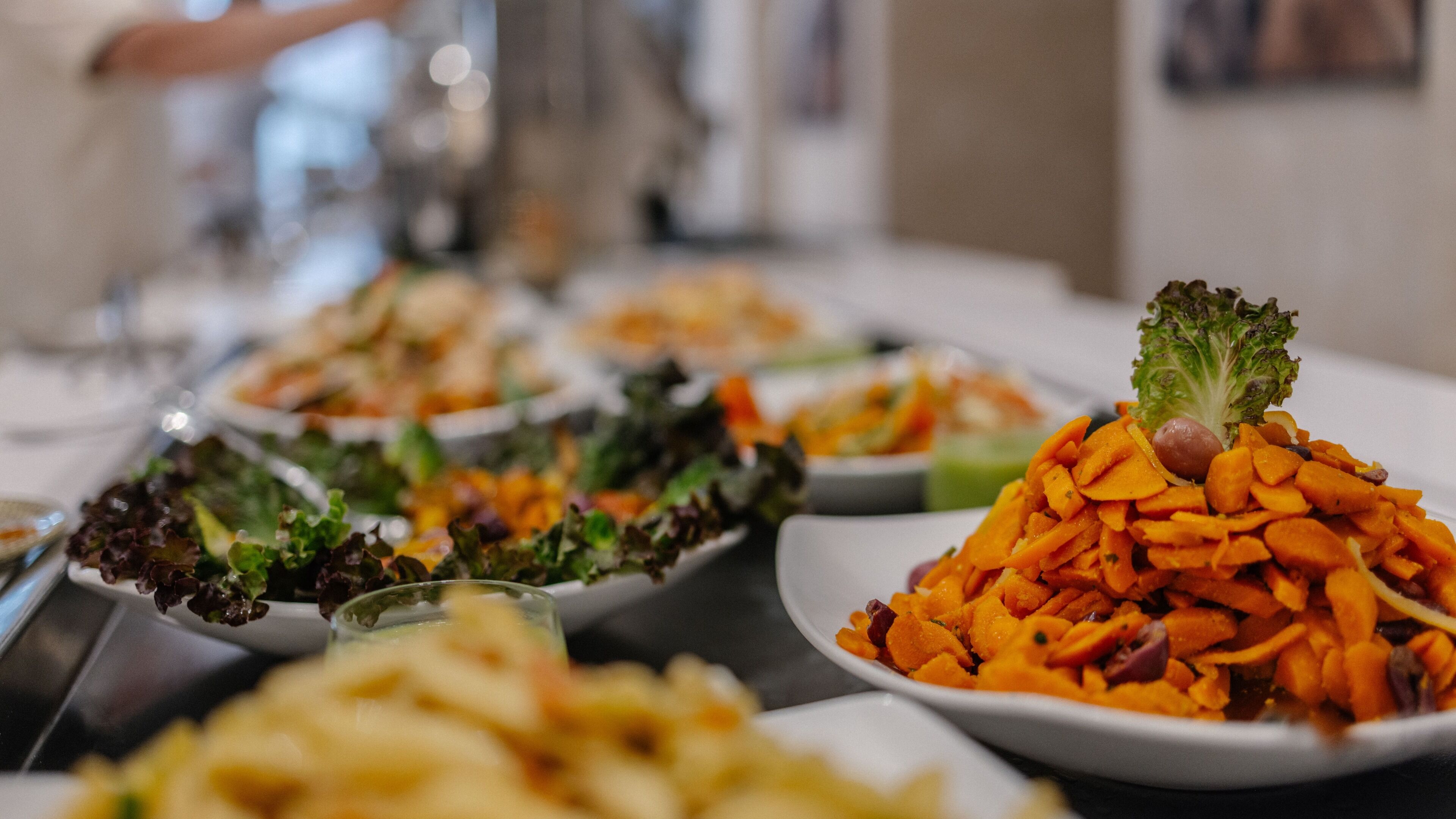 A buffet table with various dishes including a pile of sliced carrots and a salad with lettuce.