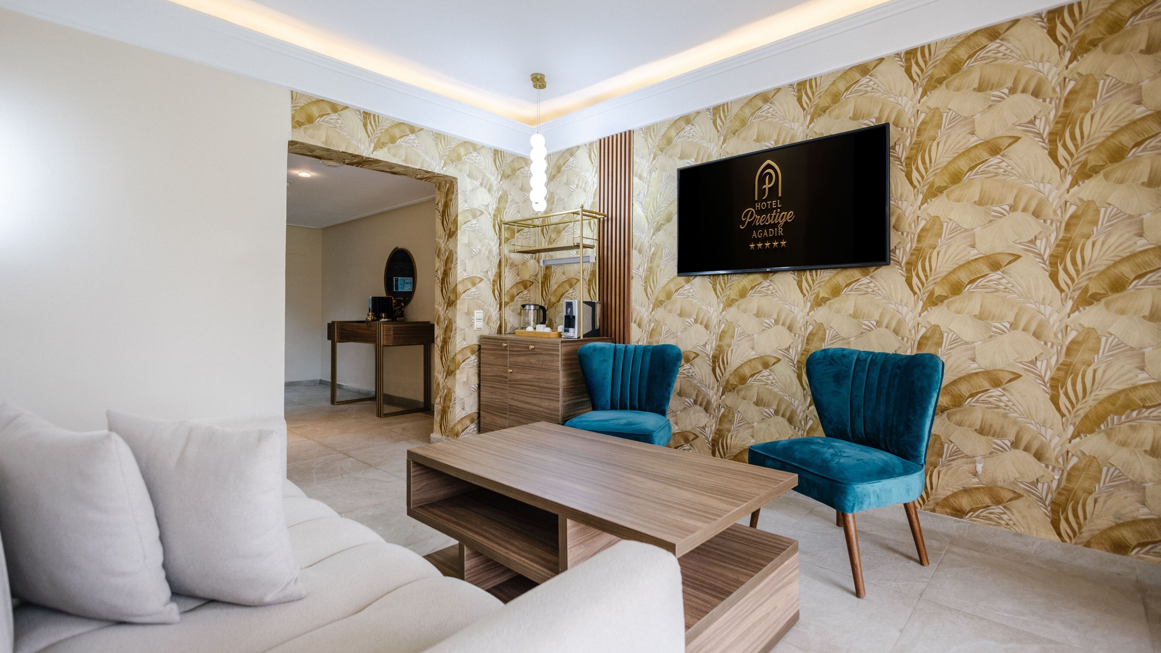 Un salon moderne comprenant un canapé, deux fauteuils, une table basse et un téléviseur fixé au mur.