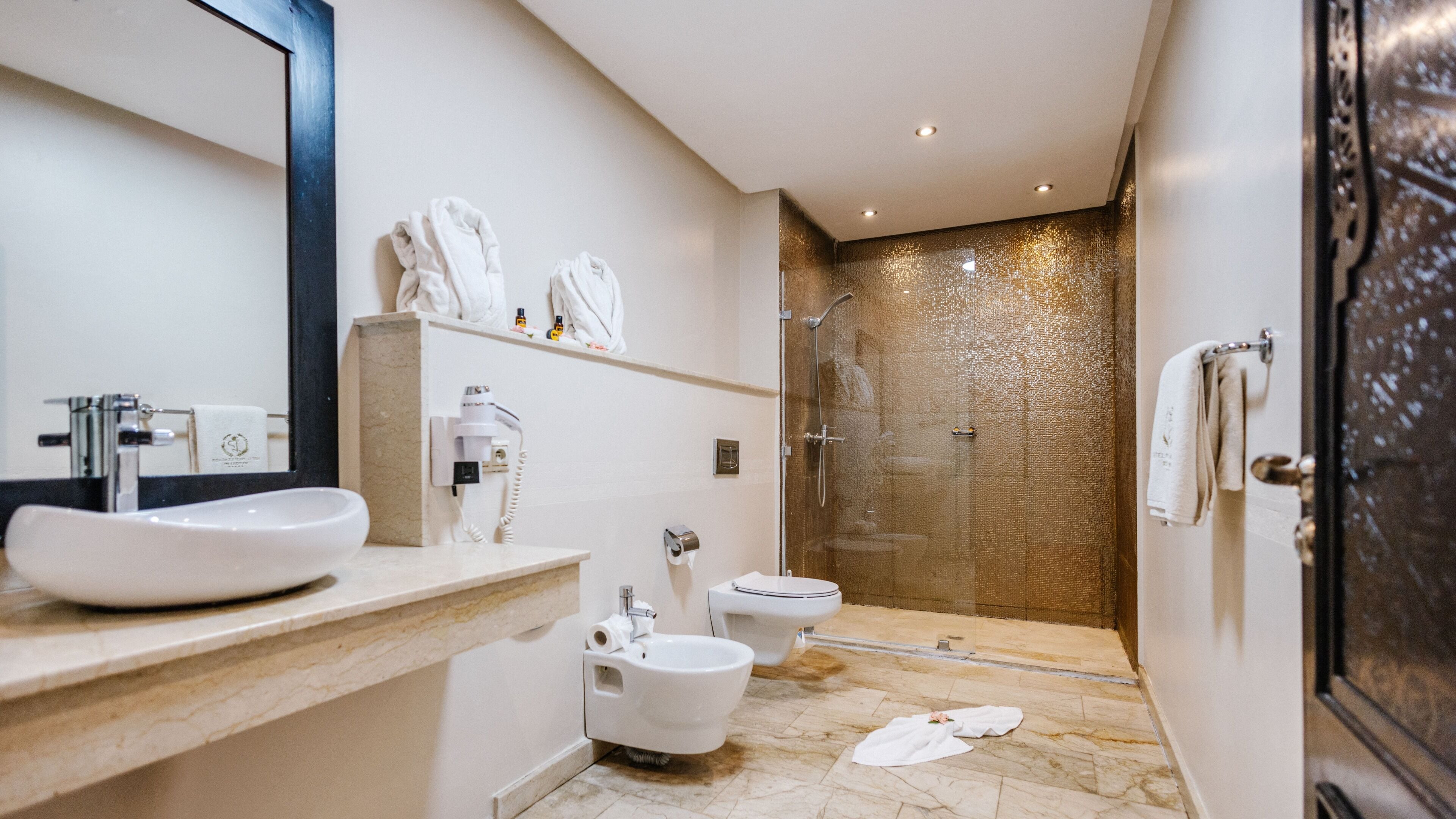 A modern bathroom with a large sink, two toilets, a bidet, and a glass-enclosed shower.