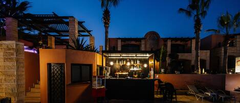 An outdoor bar area with a counter, seating, and palm trees.