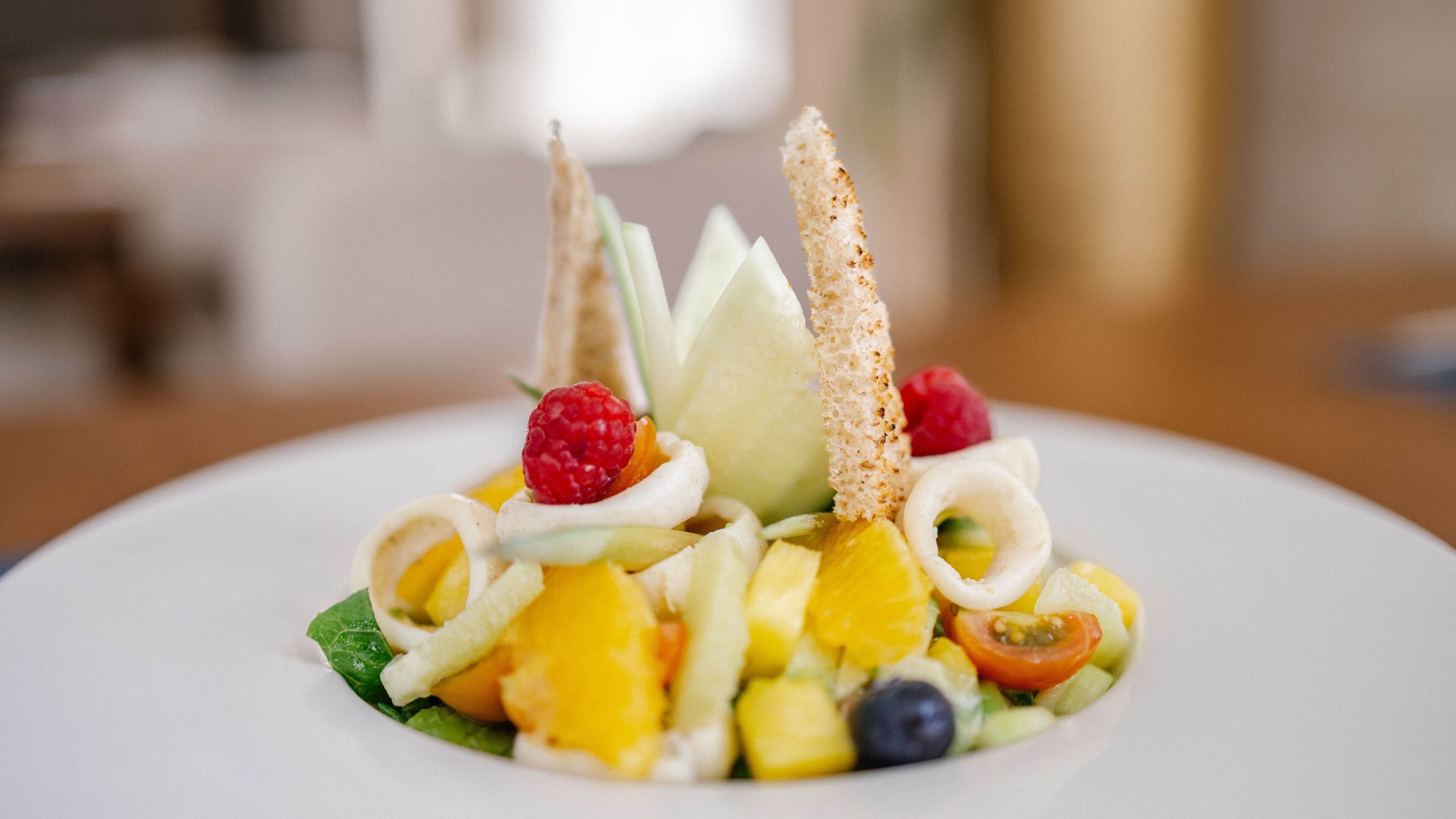 A dessert plate with various fruits, a raspberry, and a piece of bread.