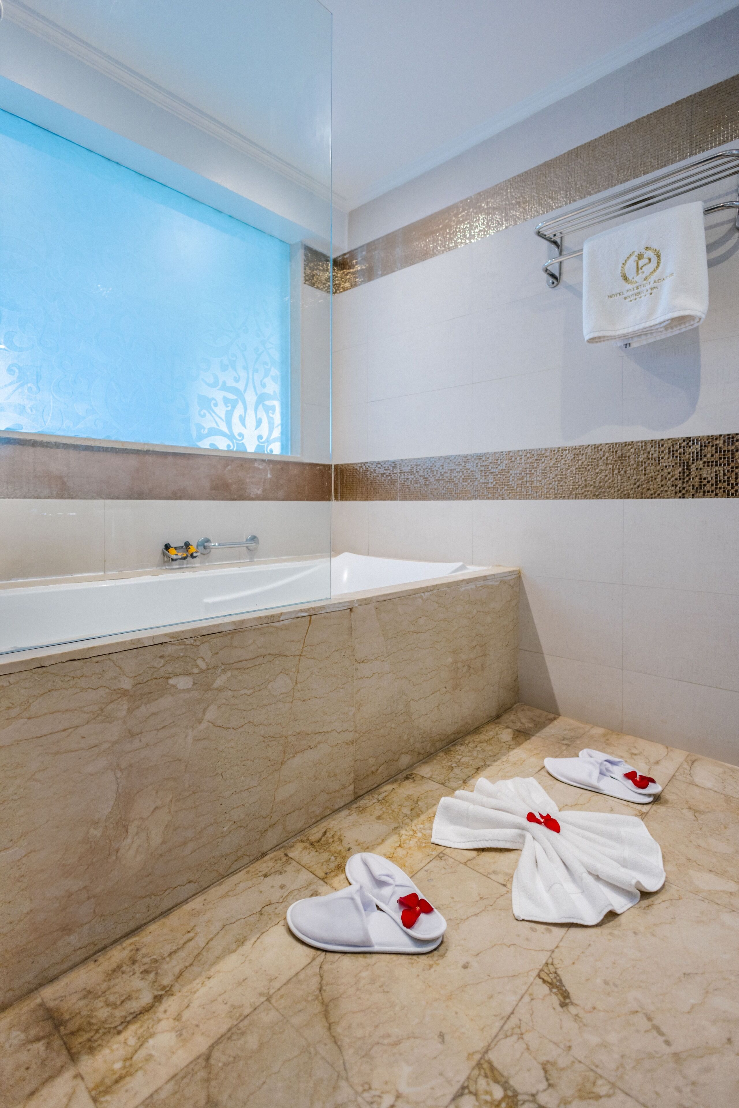 Une salle de bain avec une baignoire, un porte-serviettes avec une serviette, et une paire de chaussons sur le sol.