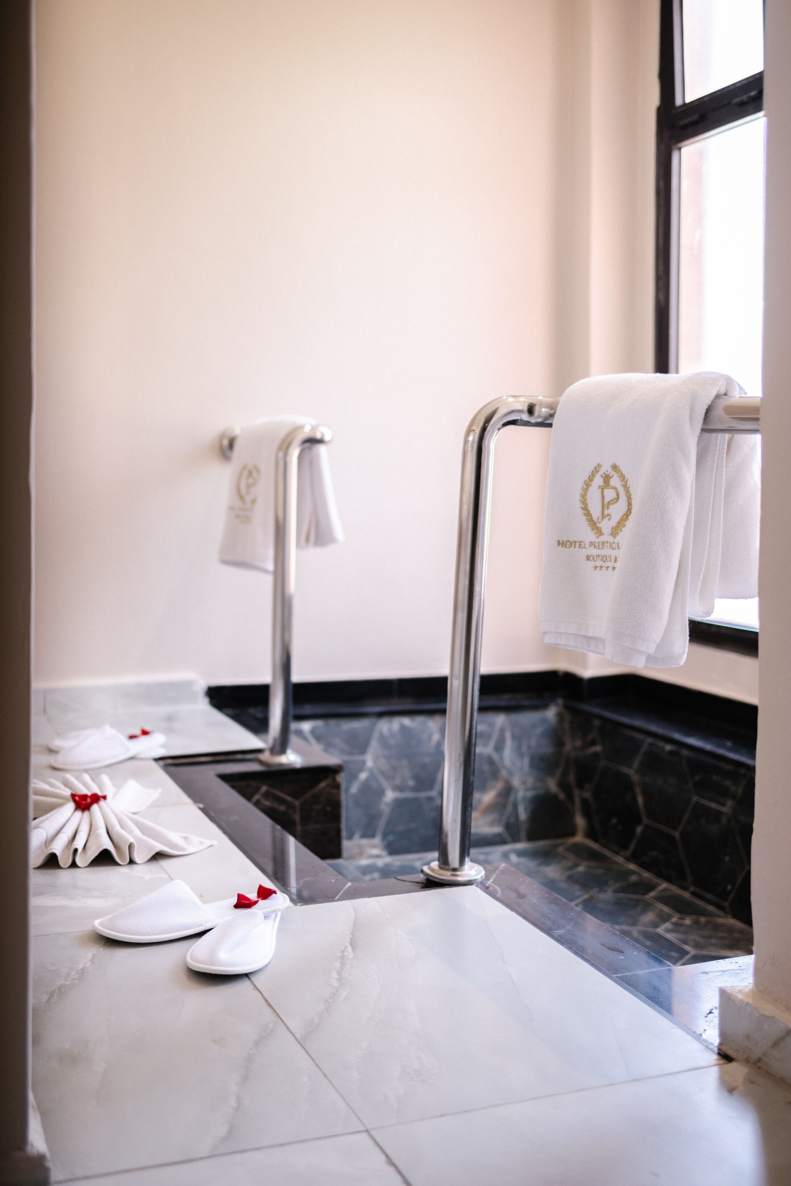 A bathroom with a marble floor, a towel rack with a towel, and a pair of slippers with a red bow.