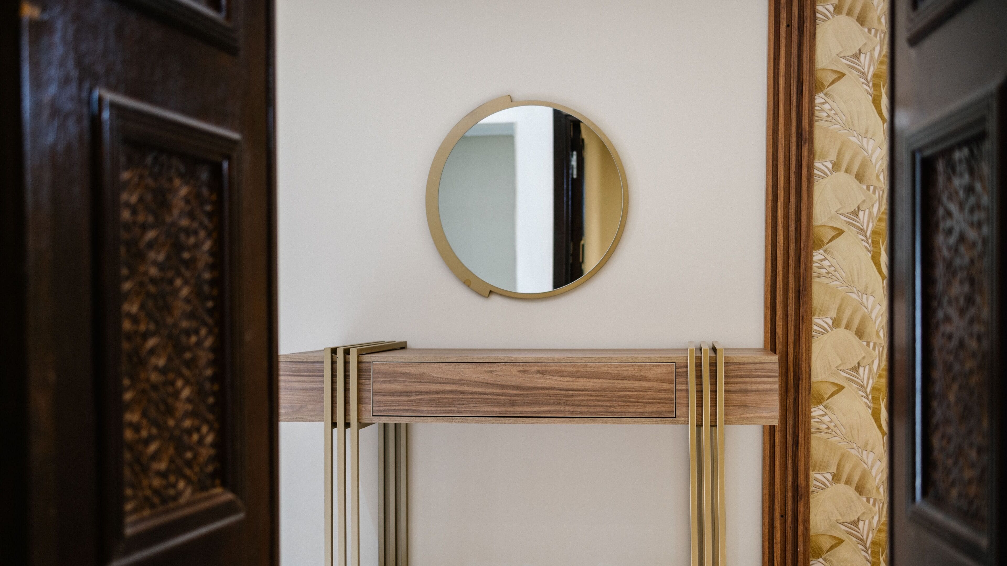 A mirror on a wall with a wooden frame and a decorative panel.