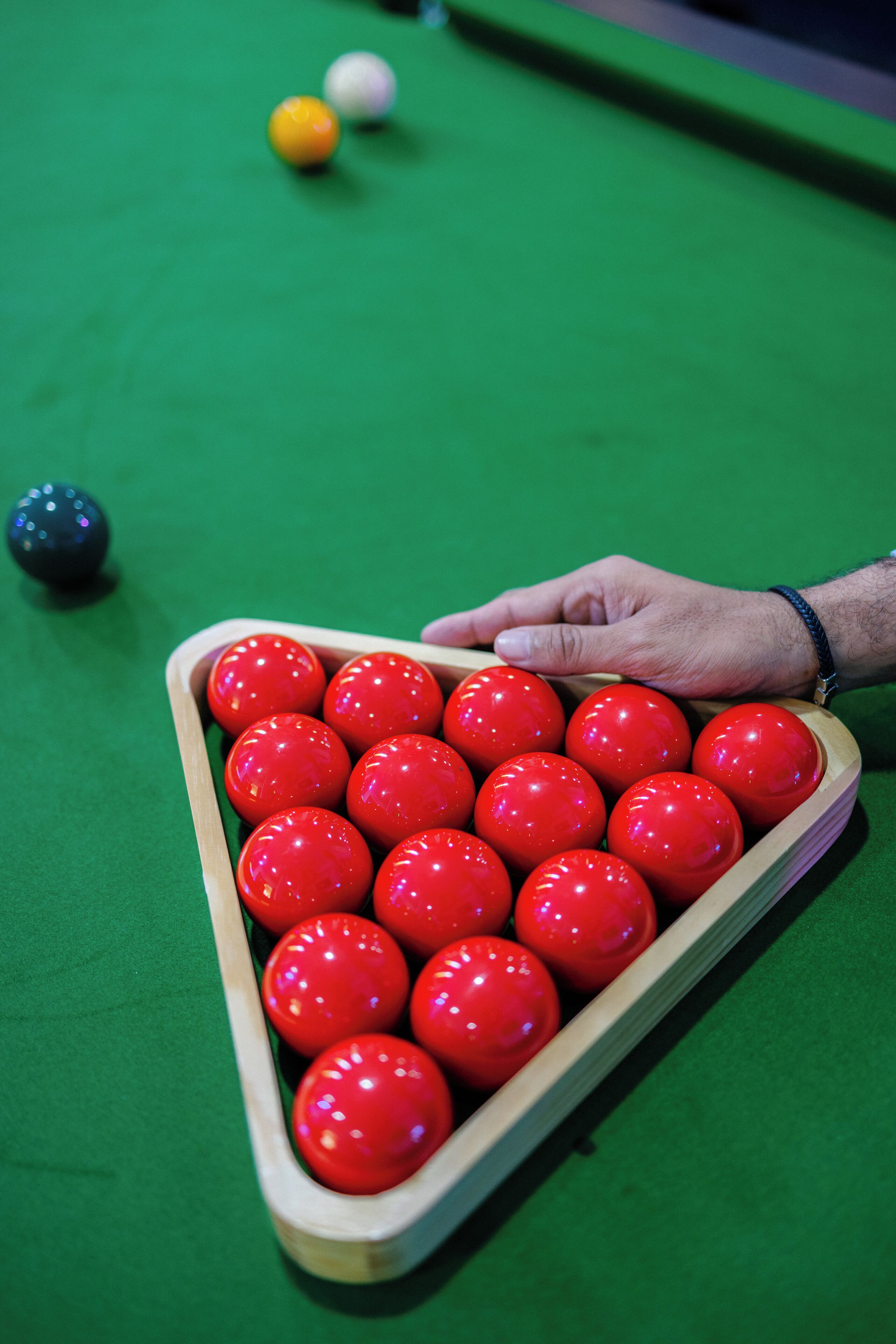 Una mesa de billar con una mano alcanzando una bola roja.