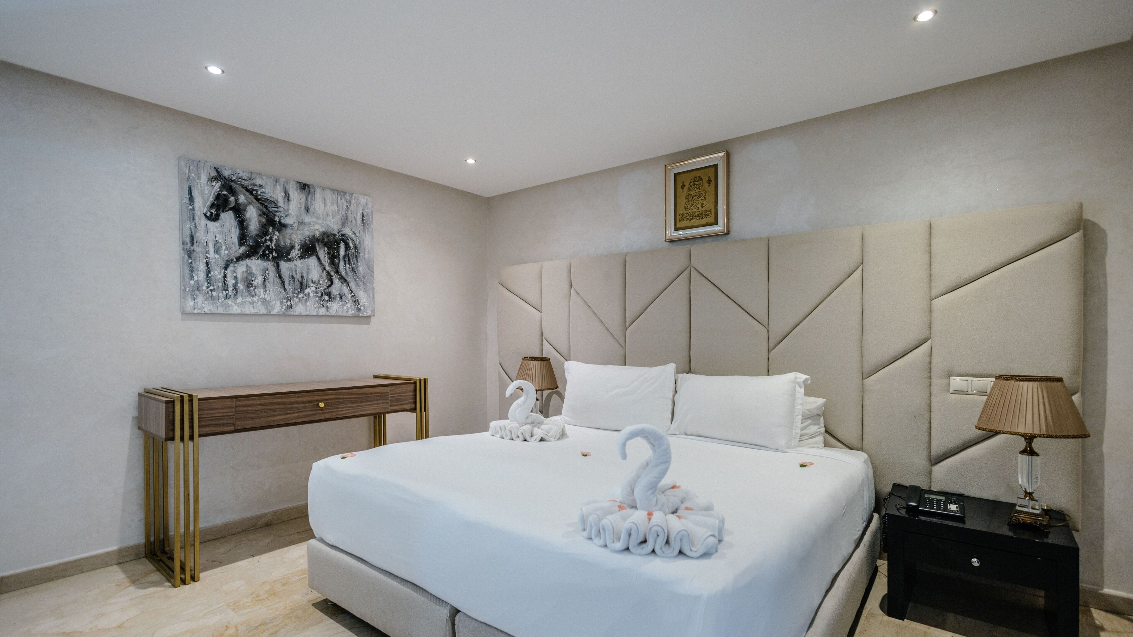 A hotel room with a large bed, a headboard with geometric patterns, a bedside table with a lamp, and a wall-mounted artwork.
