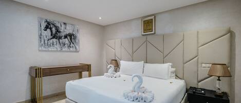 Una habitación de hotel con una cama grande, un cabecero con motivos geométricos, una mesita de noche con lámpara y una obra de arte colgada en la pared.
