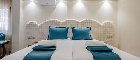 A hotel room with a large bed, two pillows, a white headboard, and an air conditioning unit on the wall.