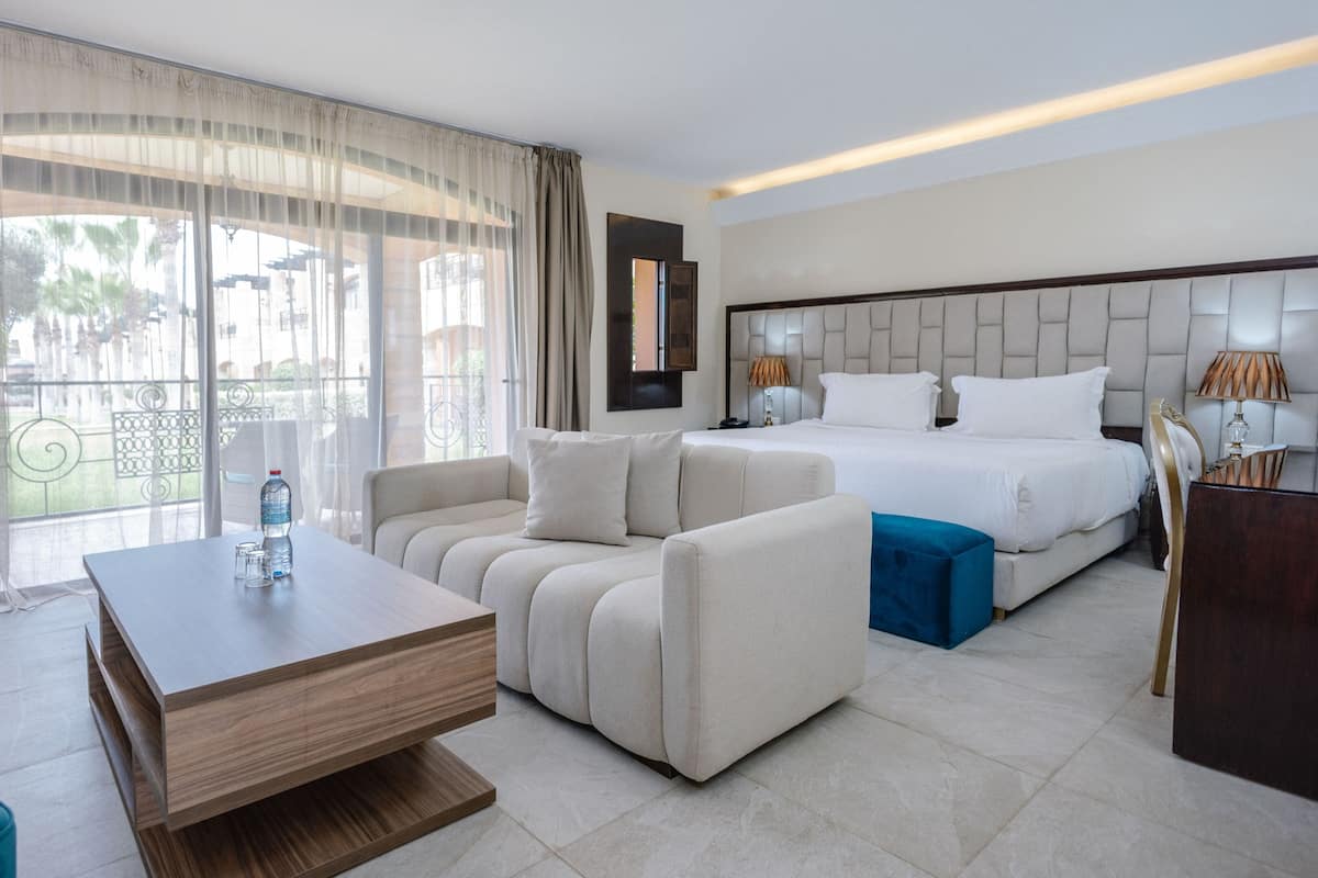 A hotel room with a bed, sofa, coffee table, and a view of the outdoors.