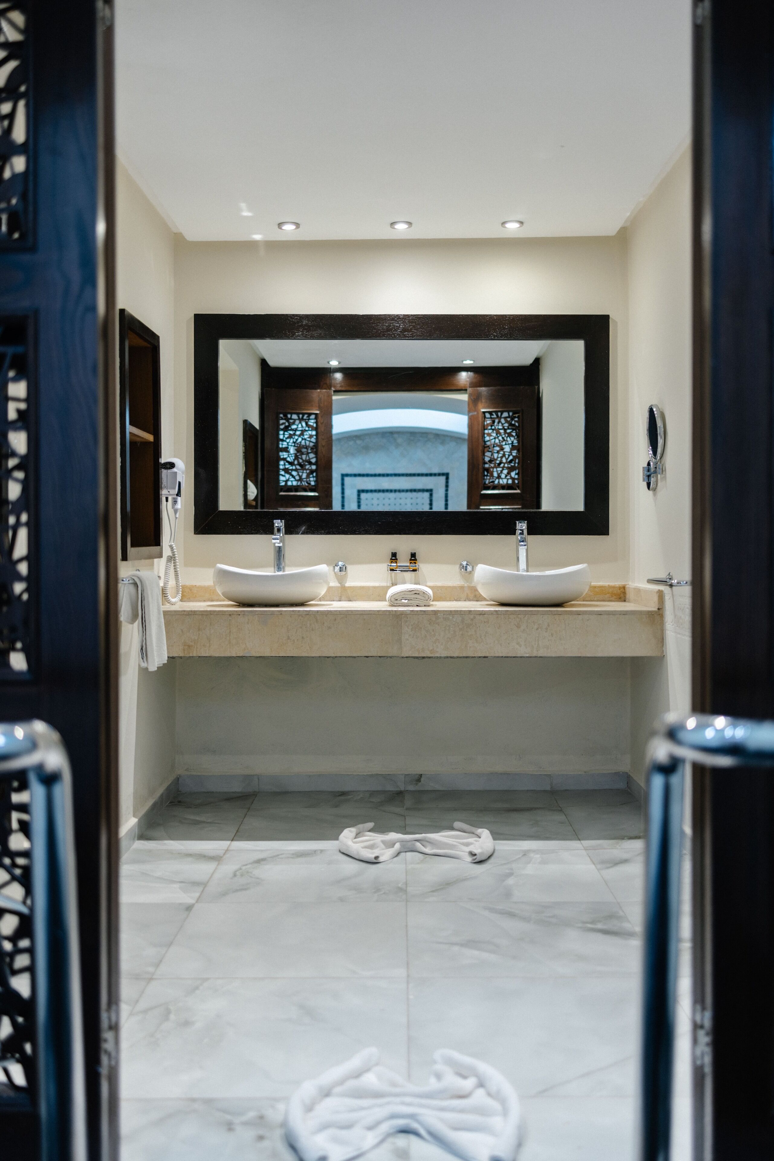 A modern bathroom with two sinks, a large mirror, and a towel rack.