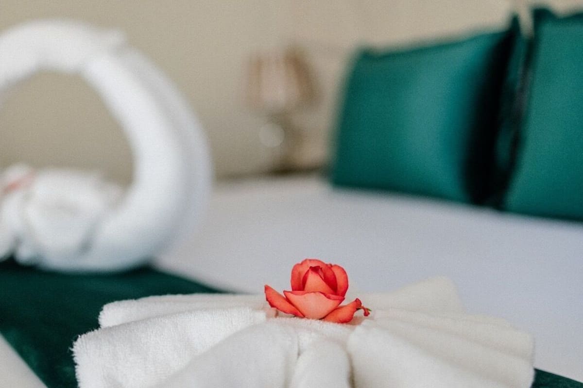 A neatly made bed with a towel and a rose.