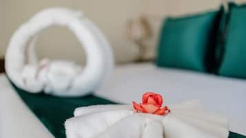 Ein ordentlich bezogenes Bett mit einem Handtuch und einer Rose.