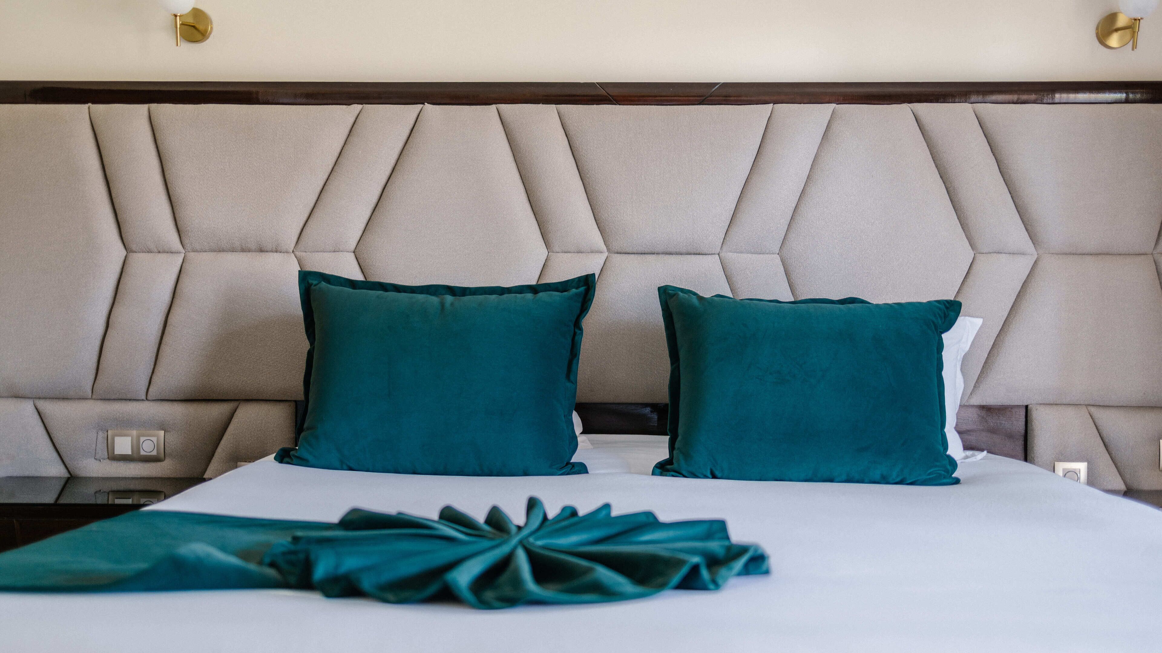 A bed with a tufted headboard, two teal pillows, and a folded teal blanket.