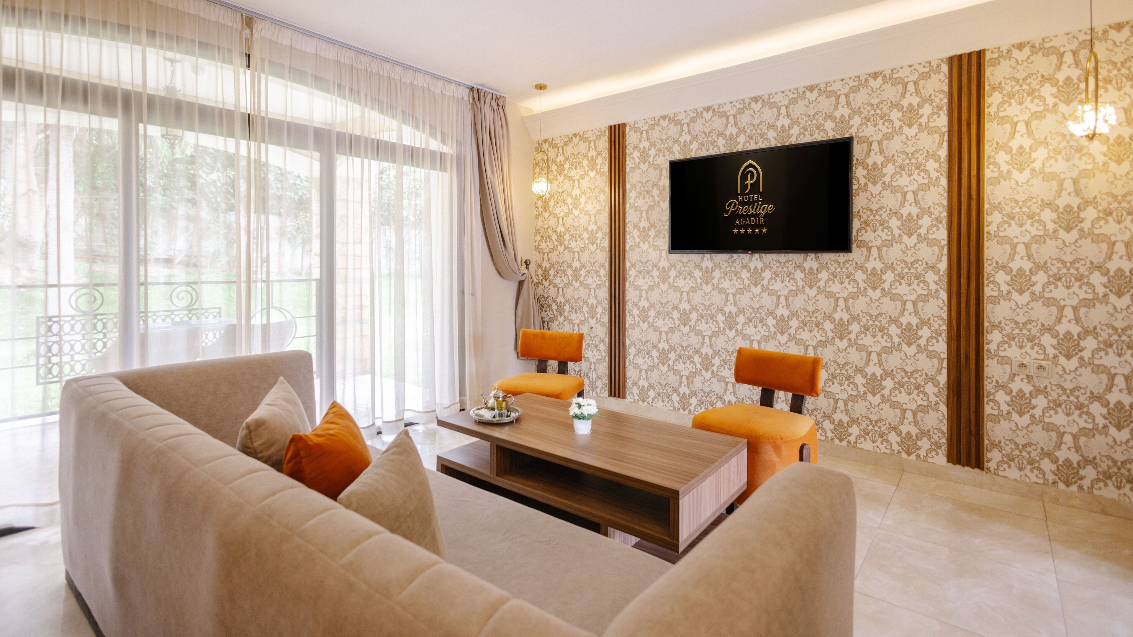 A modern hotel room with a sofa, two armchairs, a wooden coffee table, and a TV on the wall.