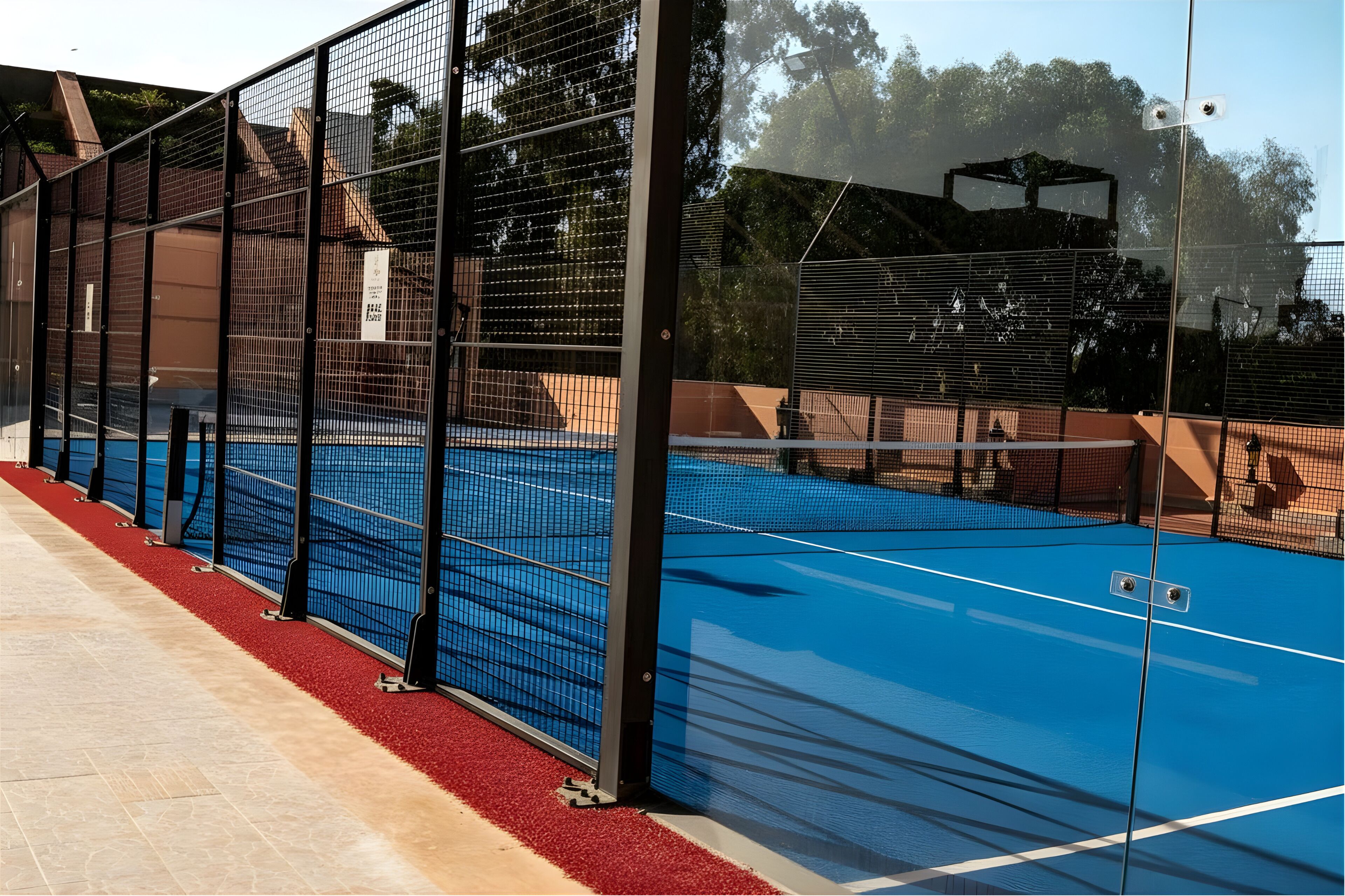 Una cancha de tenis con una red, rodeada por una valla, y un camino con alfombra roja.