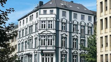Un edificio en esquina con fachada blanca y detalles oscuros, con varias ventanas y un reloj visible en el lado derecho.