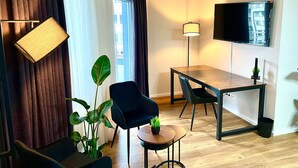 A modern hotel room with a dining area, a flat-screen TV, a floor lamp, and a potted plant. - La Plaza24 (Düsseldorf)