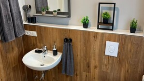 A modern bathroom with a wooden vanity, a white sink, a mirror, and a toilet. - La Plaza24 (Düsseldorf)