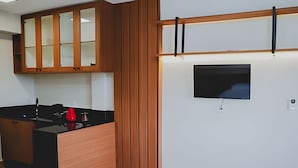 A modern kitchen with wooden cabinets, a black countertop, and a red vase. - Loft completo e climatizado (Cuiabá)