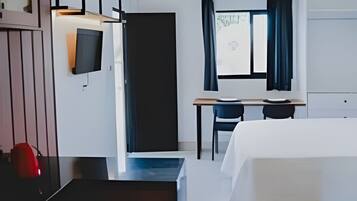 A hotel room with a bed, a desk, a chair, a TV mounted on the wall, and a window with curtains.