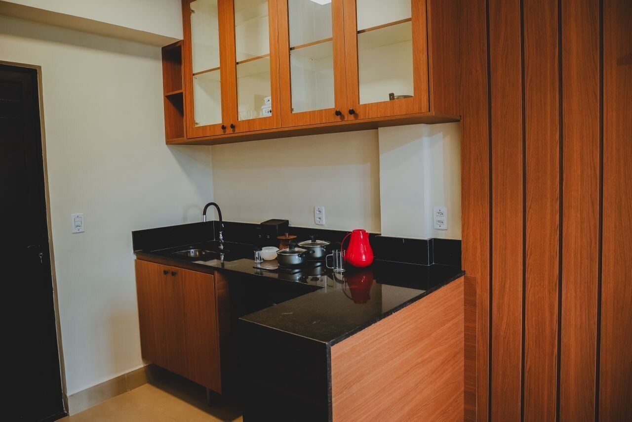 Una cocina compacta con armarios de madera, encimera negra y hervidor rojo.