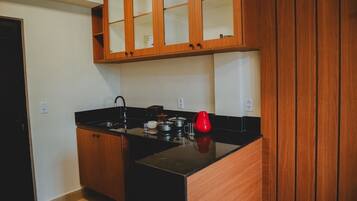 Una cocina compacta con armarios de madera, encimera negra y hervidor rojo.