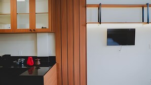 A modern kitchen with wooden cabinets, a black countertop, and a red kettle. - Loft completo e climatizado (Cuiabá)