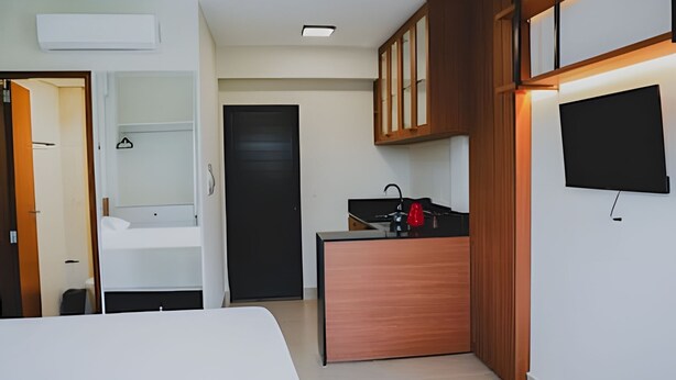 A compact hotel room with a bed, a small kitchenette, a TV, and a wardrobe. - Loft completo e climatizado (Cuiabá)
